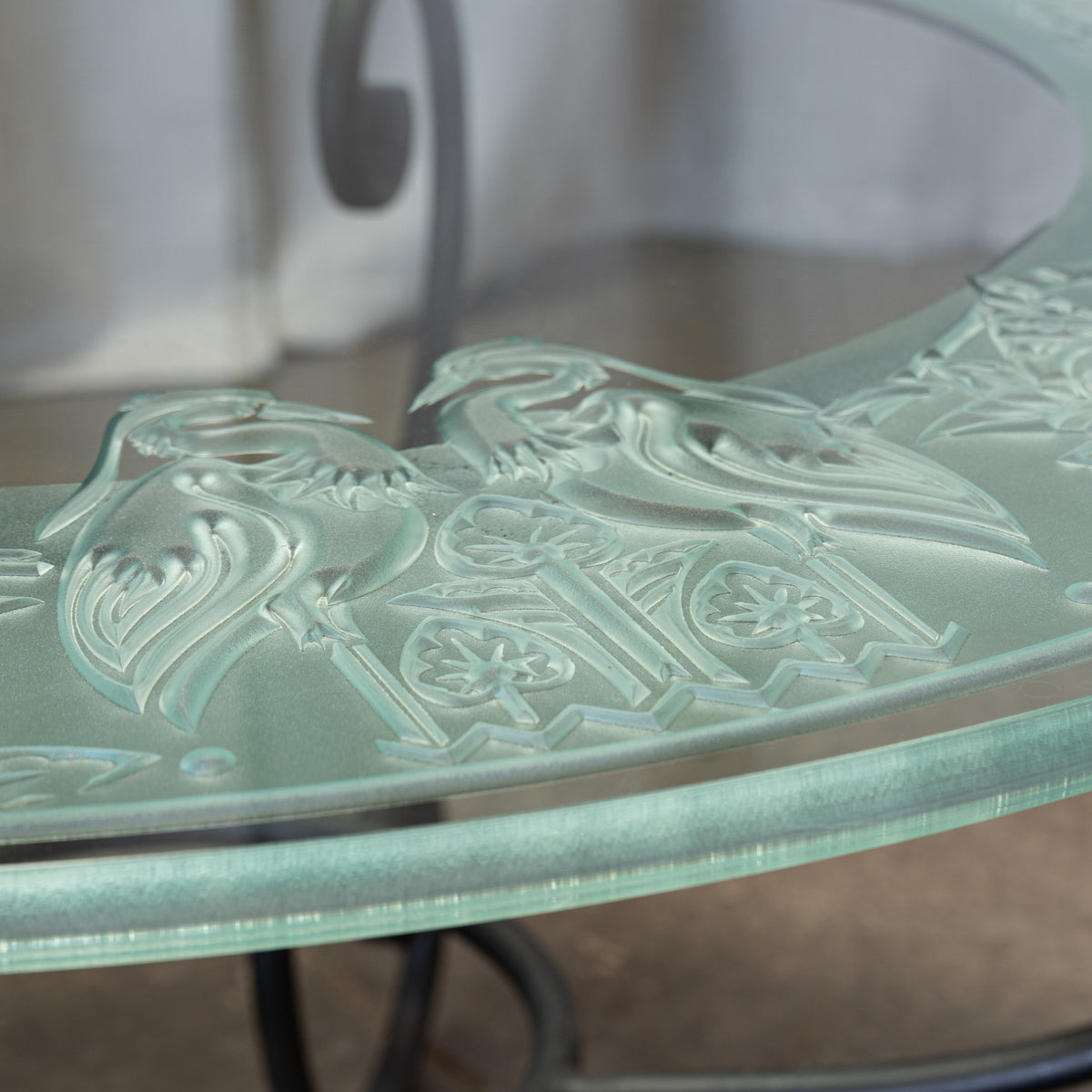 Close-up of a frosted glass tabletop with an embossed floral and scroll pattern, showing a pale mint-green tint and reflective surface.