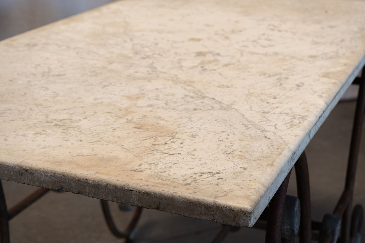 A close-up view of a rectangular stone tabletop with a warm beige and cream marbled surface, supported by dark metal legs.