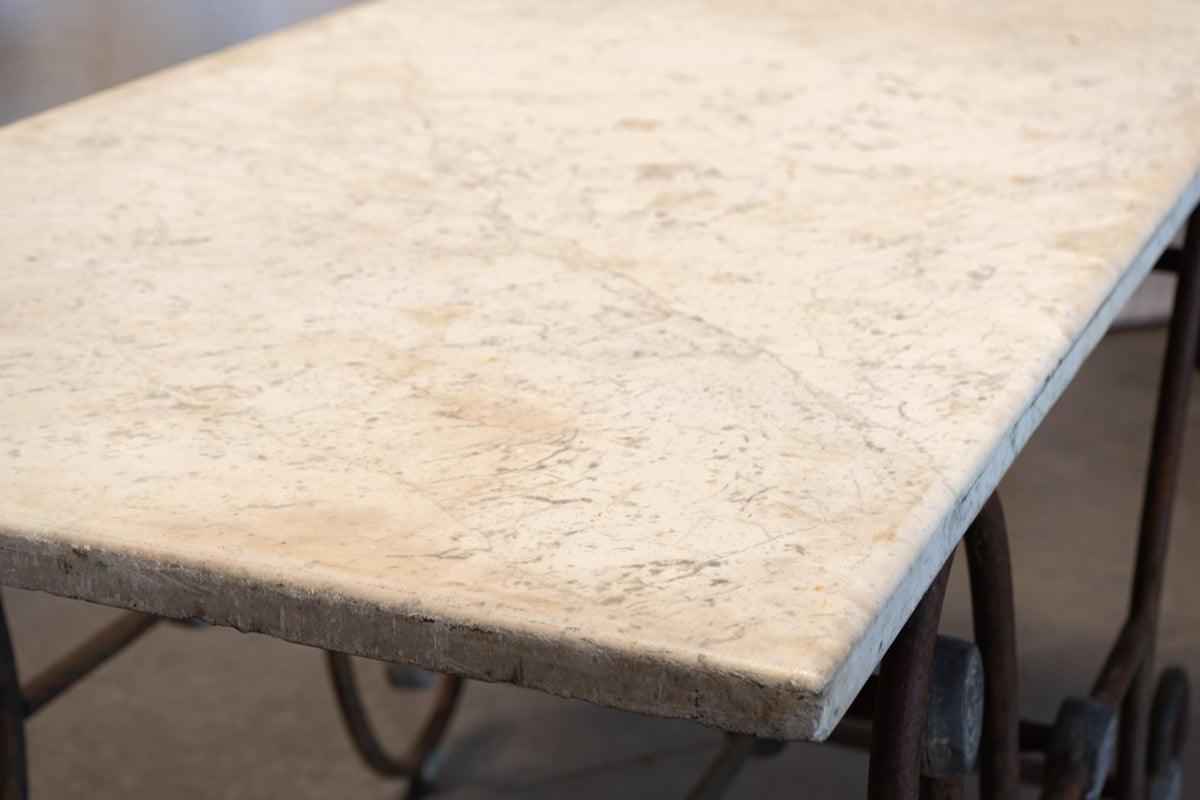 A close-up of a rectangular table top made of light beige stone with natural marbled veining, supported by dark metal legs.