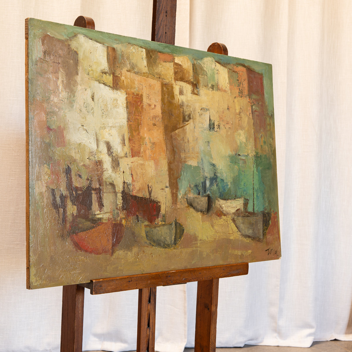 An abstract canvas painting displayed on a wooden easel against a draped white fabric backdrop. The painting features a textured, blocky composition in earthy tones of beige, brown, green, and orange.