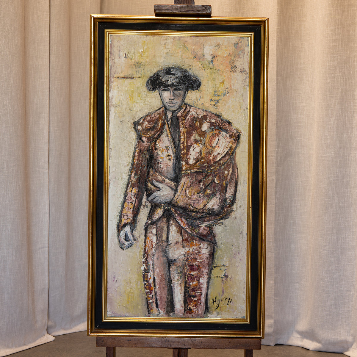 A framed vertical painting on an easel, depicting a man in a textured brown and beige suit against a light background, enclosed in a gold frame.