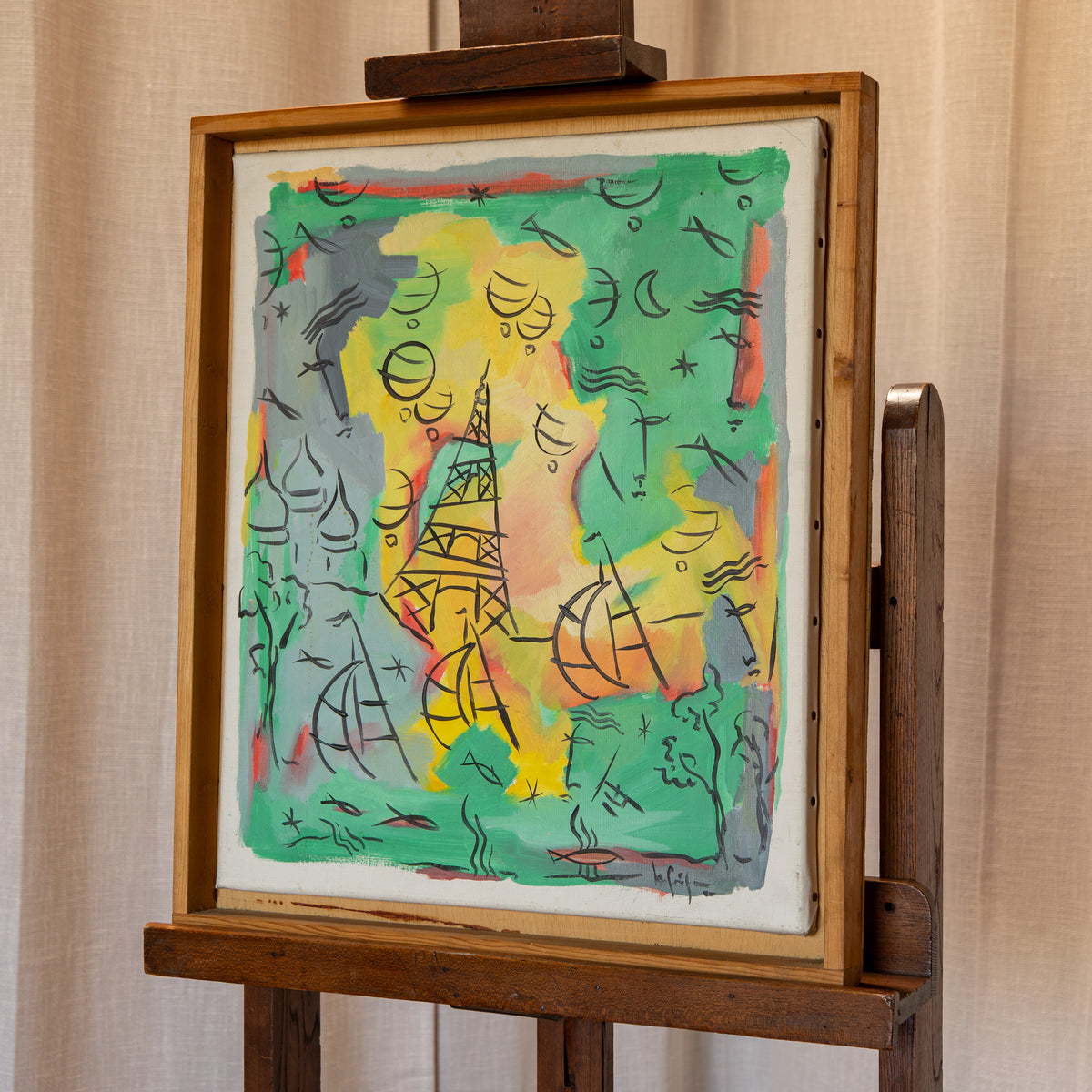 A framed abstract painting displayed on a wooden easel against a beige curtain backdrop. The artwork features a colorful composition with green, yellow, orange, and gray areas outlined in black linework.