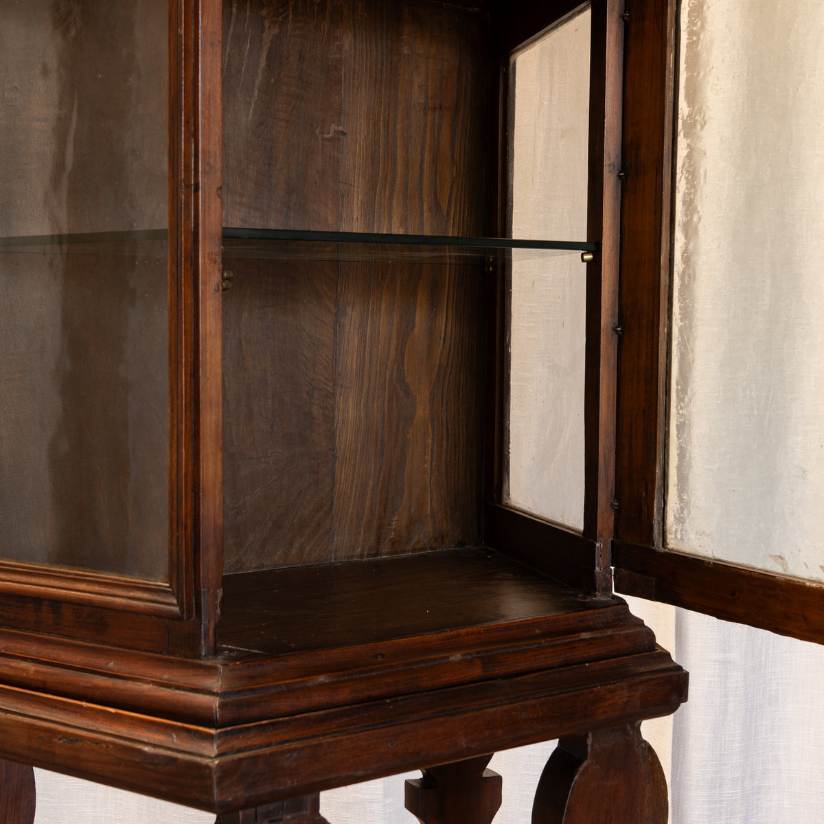 Close-up of a dark wood display cabinet with glass doors and interior glass shelves, shown against a light neutral wall.