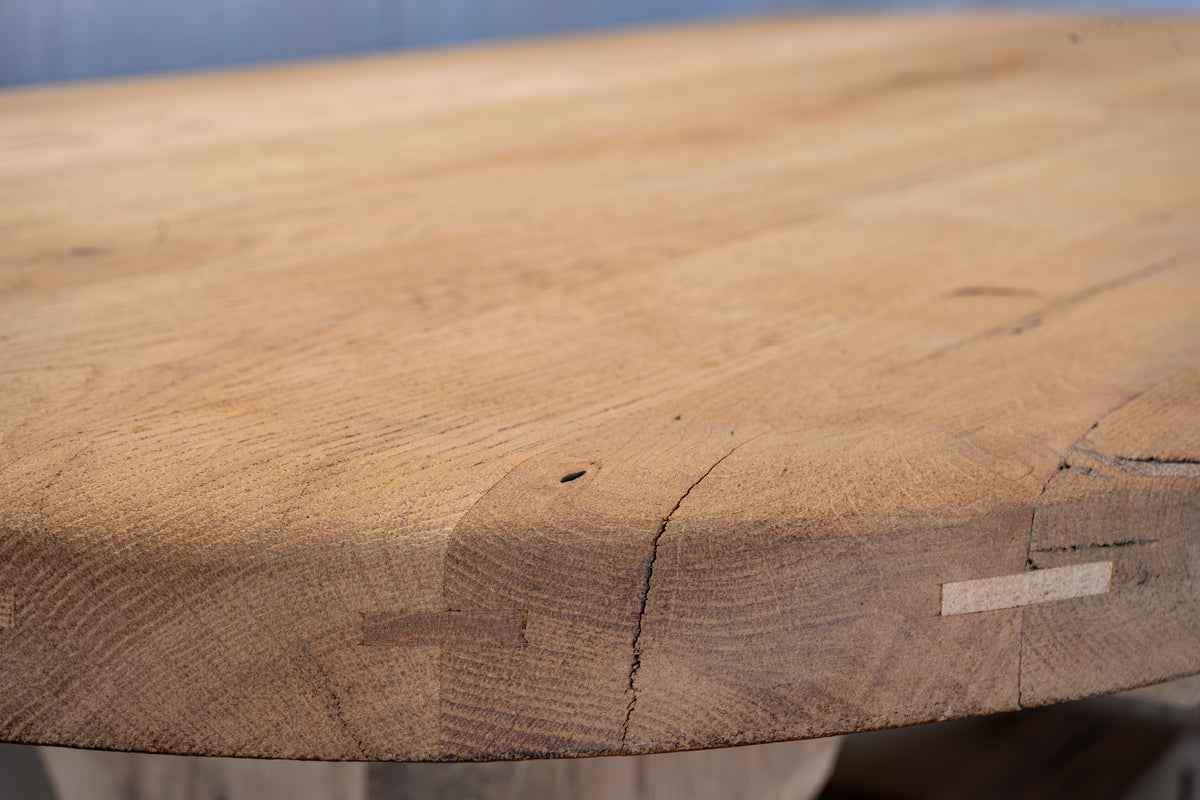 Close-up of a rustic live-edge wooden tabletop showing natural grain, knots, and a small maker's mark on the side.