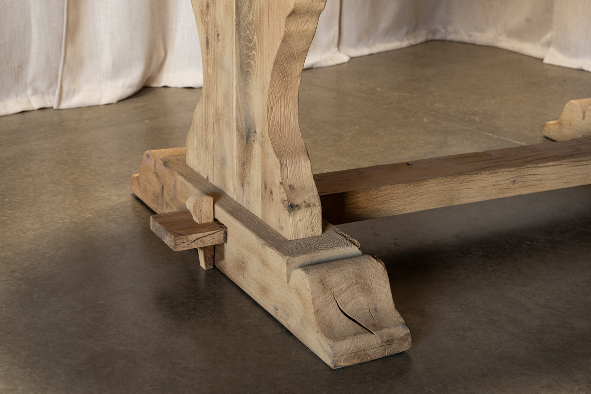 Close-up of the carved wooden legs and stretcher base of a rustic dining table, showing natural wood grain and joinery details on a concrete floor.
