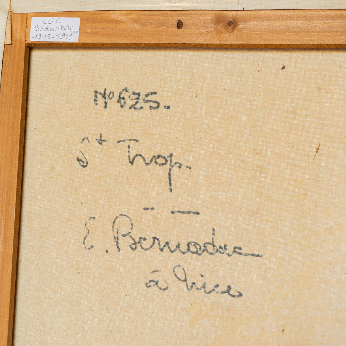 Close-up of the back of a framed artwork or print, showing beige fabric backing with handwritten markings in dark ink and a wooden frame border.