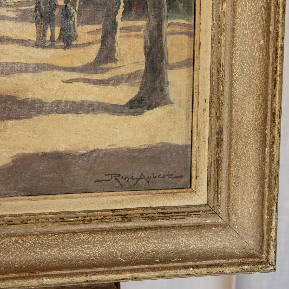 Close-up of a framed painting showing part of a park scene with tree trunks, sandy ground, and a signature near the bottom, surrounded by an ornate distressed gold frame.