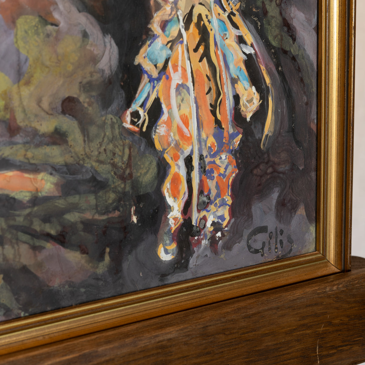 A close-up of a framed painting showing a colorful abstract horse figure in orange, blue, yellow, and white brushstrokes against a dark gray and green background, with a gold frame and a wooden surface below.