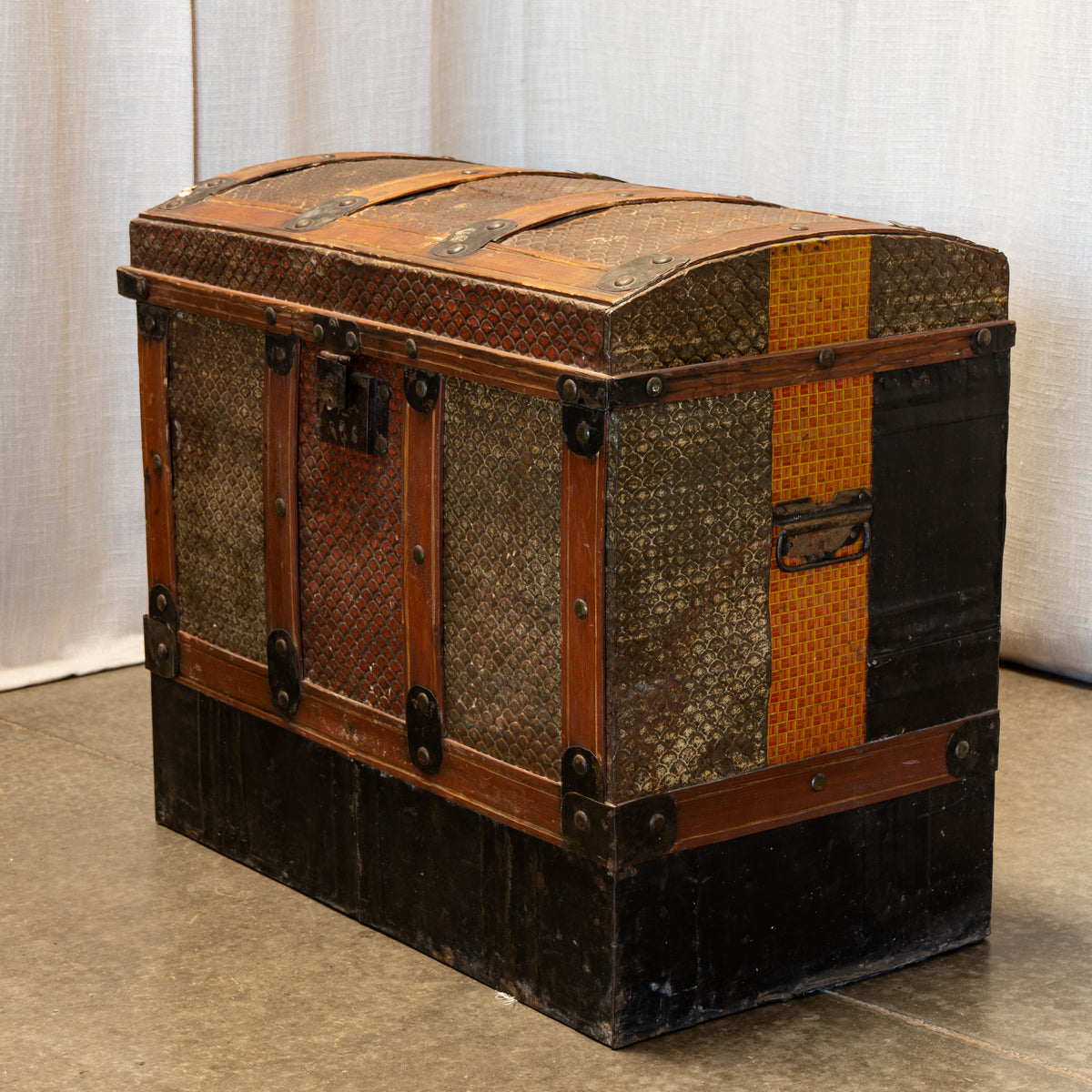 A vintage wooden trunk chest with woven patterned panels, dark metal corner protectors, and a hinged lid, photographed indoors against a light curtain backdrop.