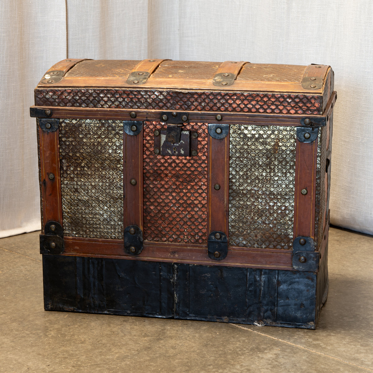 An antique wooden trunk chest with metal mesh panels and dark metal hardware, photographed against a neutral draped fabric backdrop.