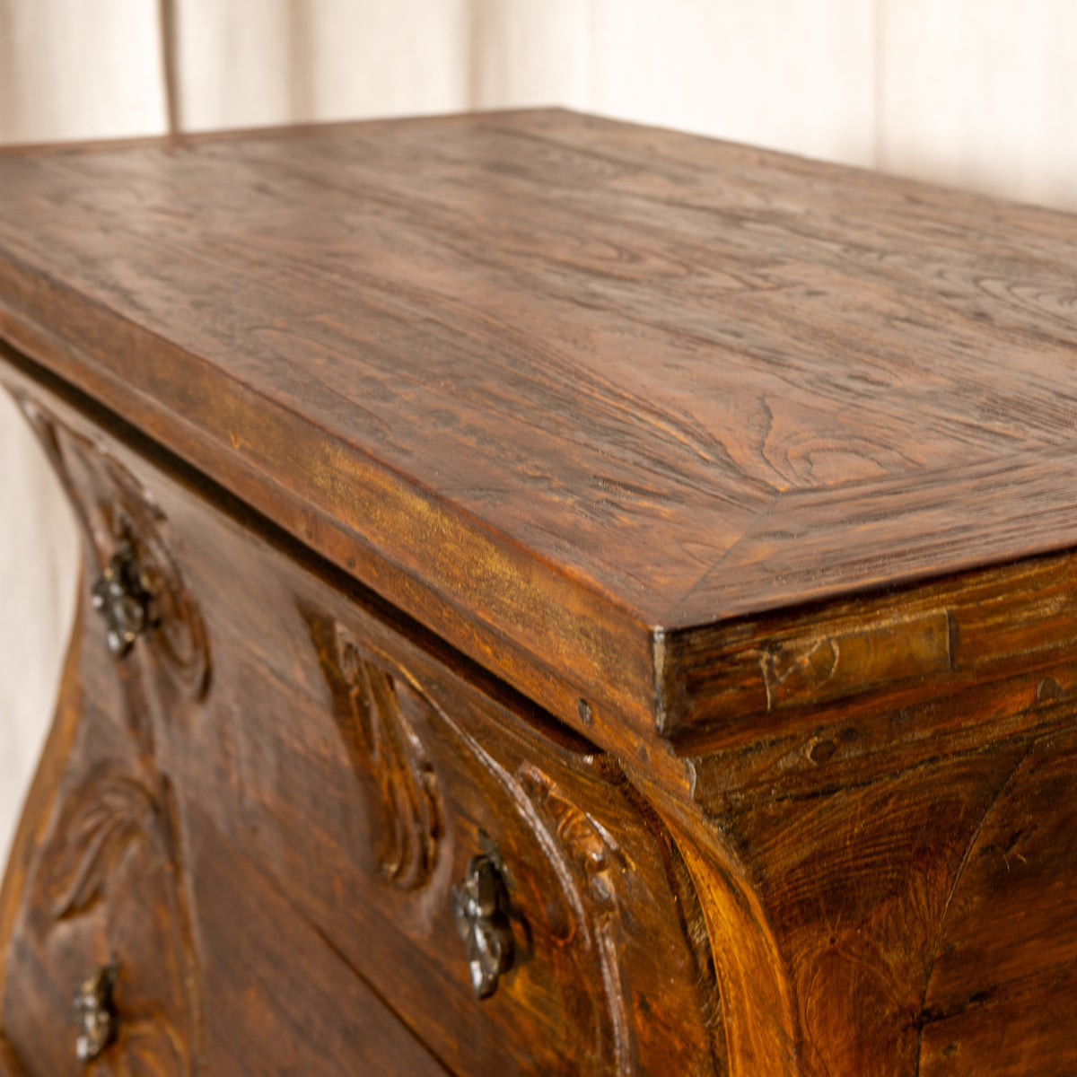 Close-up of a Jason Scott angelina dresser piece of furniture. A wooden chest of drawers with ornate carved details and dark metal drawer pulls, showing the rich wood grain on the top and front.