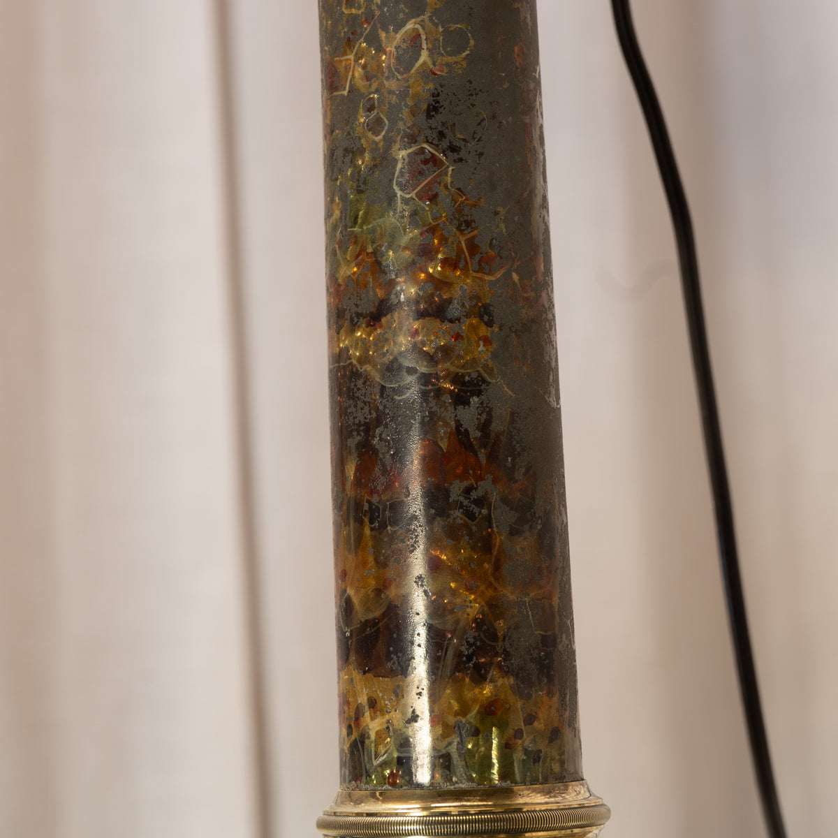 A close-up of a cylindrical lamp base featuring a textured, crackled dark glass column filled with amber and gold glitter, set against a neutral light background.