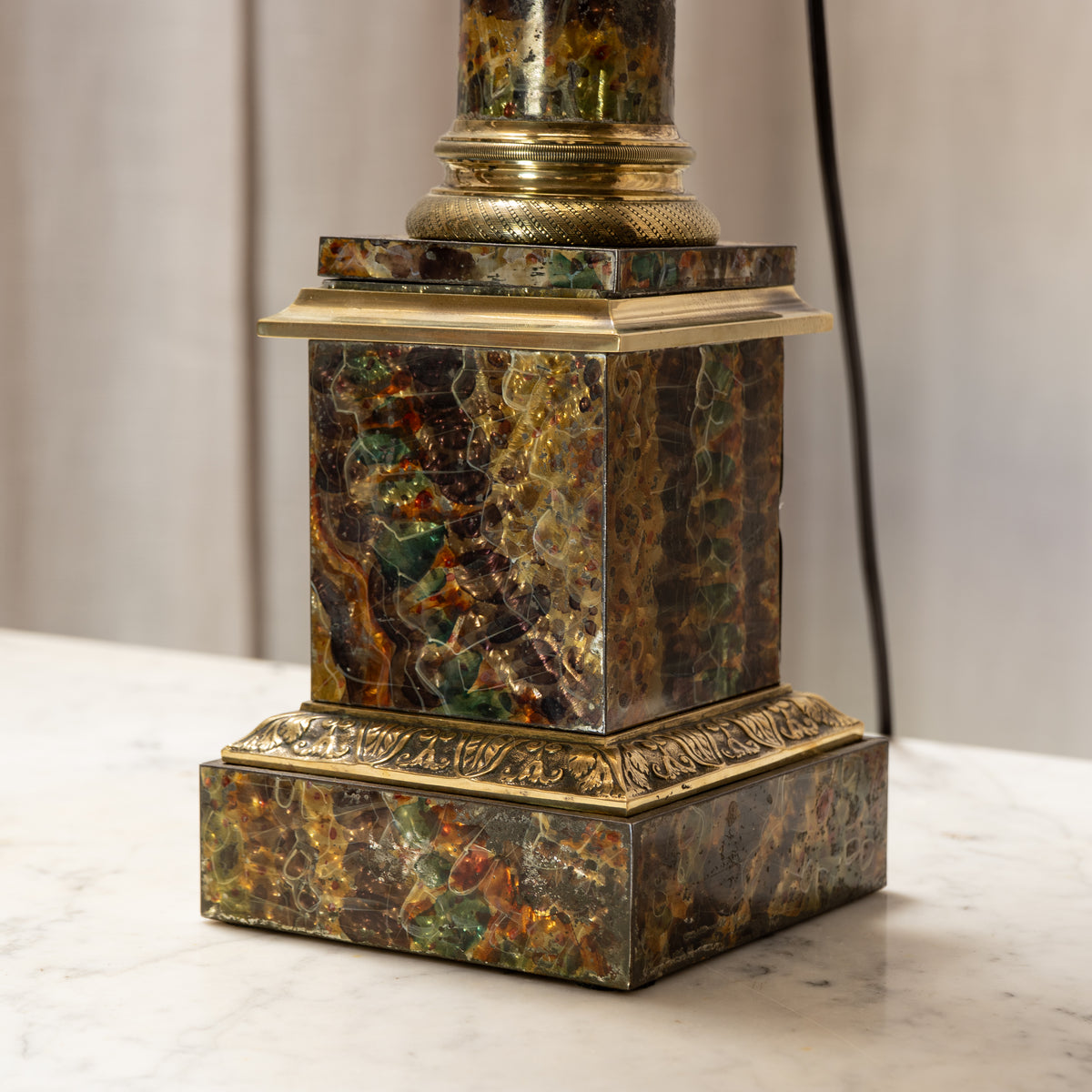 An ornate vintage table lamp featuring a square pedestal base made of marbled green, gold, and brown stone, accented with brass gilded trim and a matching gold-toned lampshade collar.