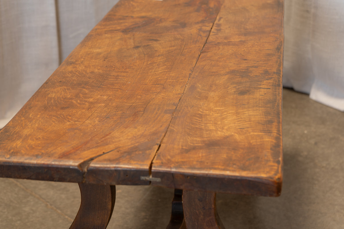 Close-up of a rustic wooden table with a richly stained brown finish, showing natural wood grain and a visible crack along the tabletop seam.