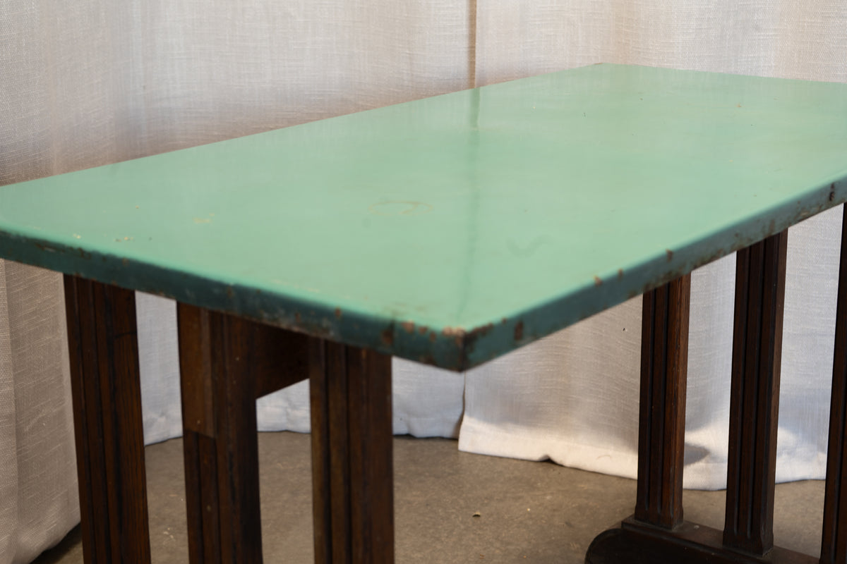 A rectangular table with a distressed mint green top and dark brown wooden legs, photographed against a draped white fabric backdrop.