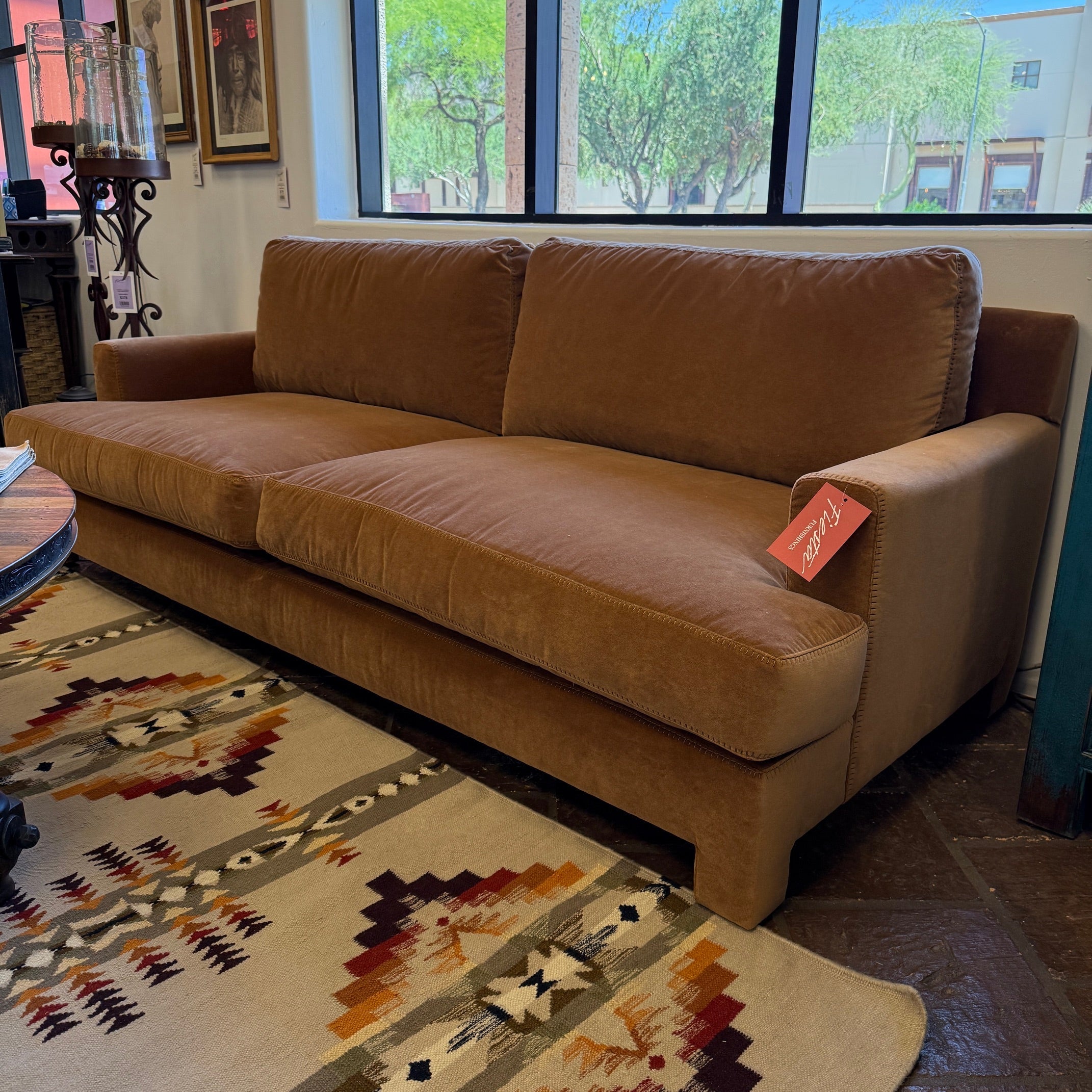 Brown sofa with a tag in a room with large windows and a patterned rug.