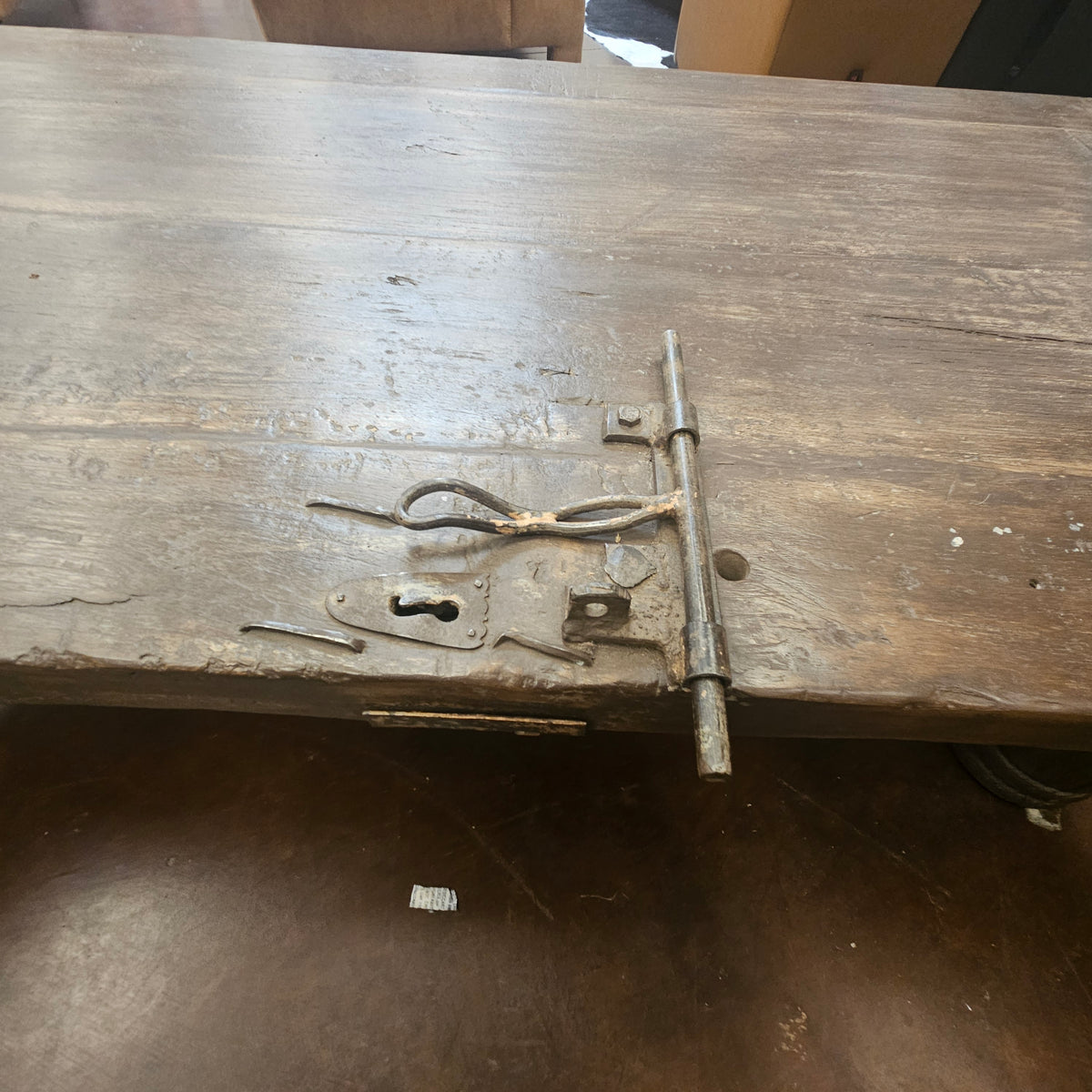 A rustic wooden table or bench with a heavy-duty metal latch and lock mechanism on the side, photographed in a workshop or storage setting.