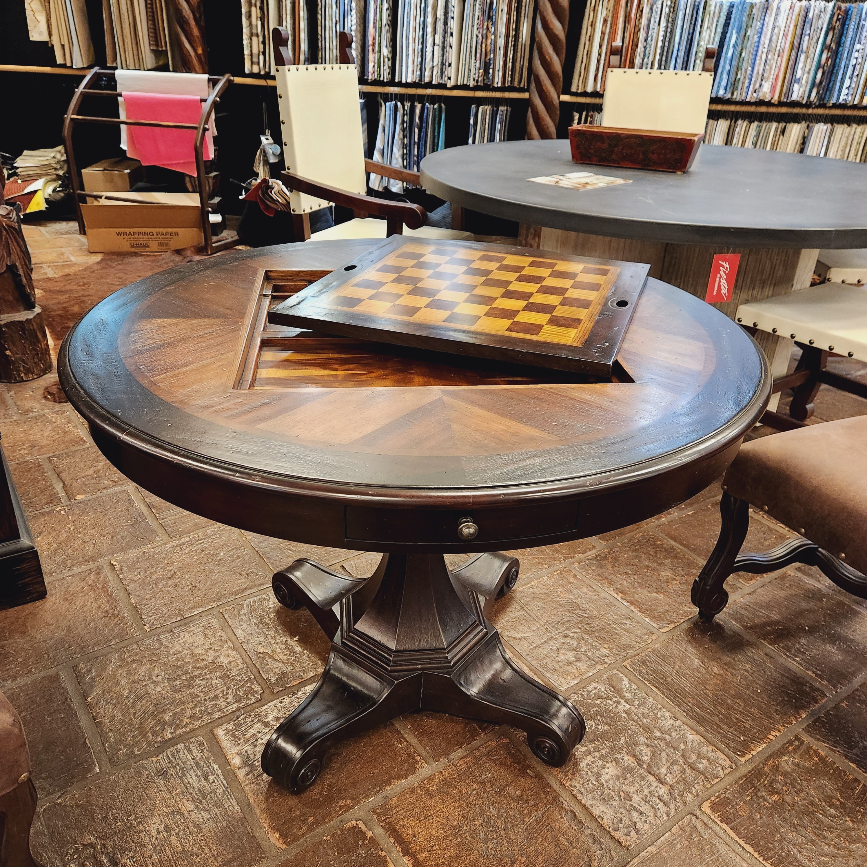 Round wooden table with a checkered board on top in a room with bookshelves.