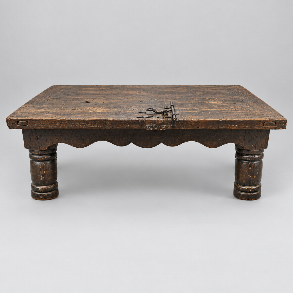 A rustic dark brown wooden low table with a scalloped apron and four turned legs, featuring a metal latch on the front, photographed on a light gray background.